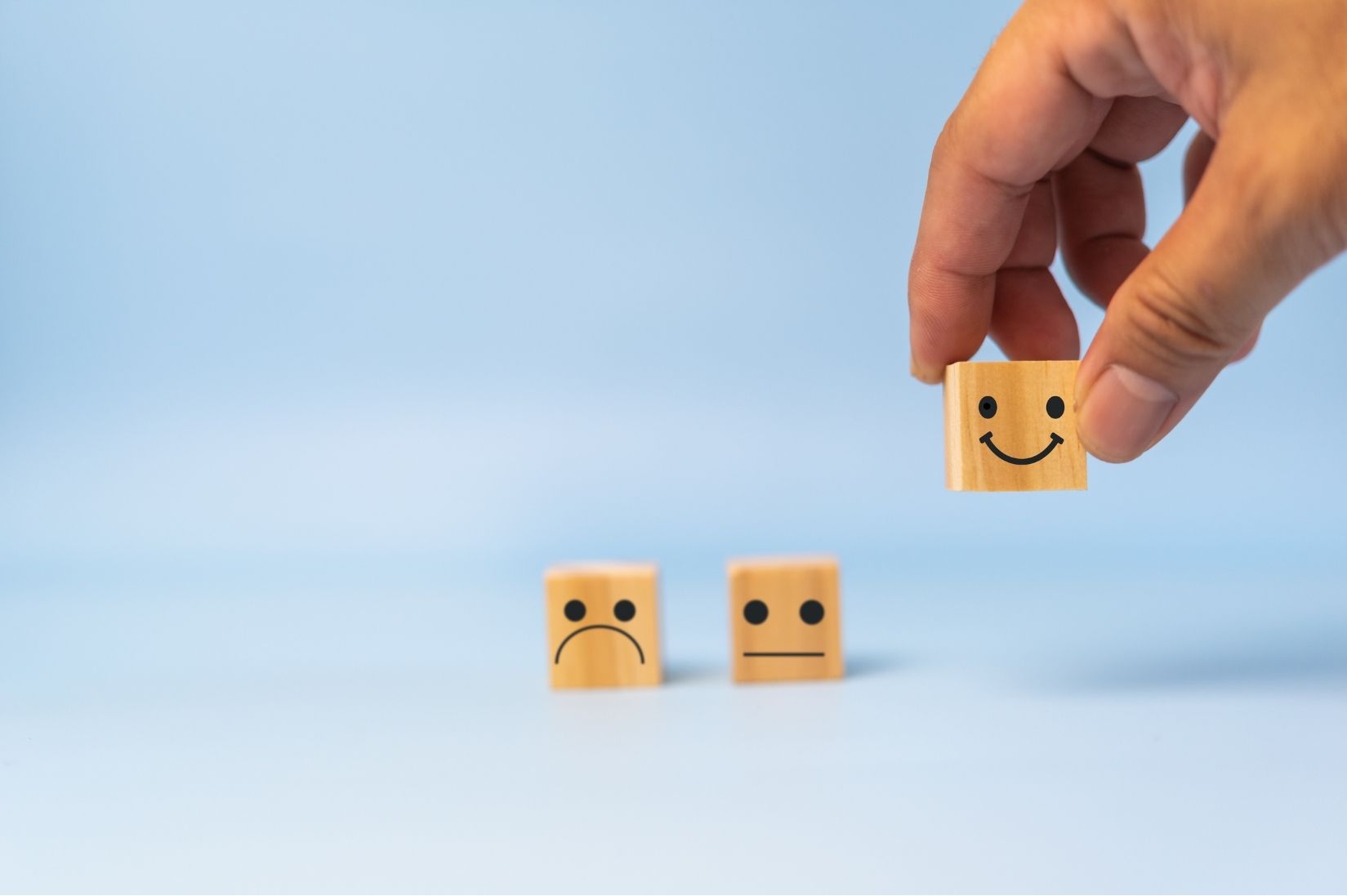 A hand placing a smiling wooden block in front of sad and neutral ones