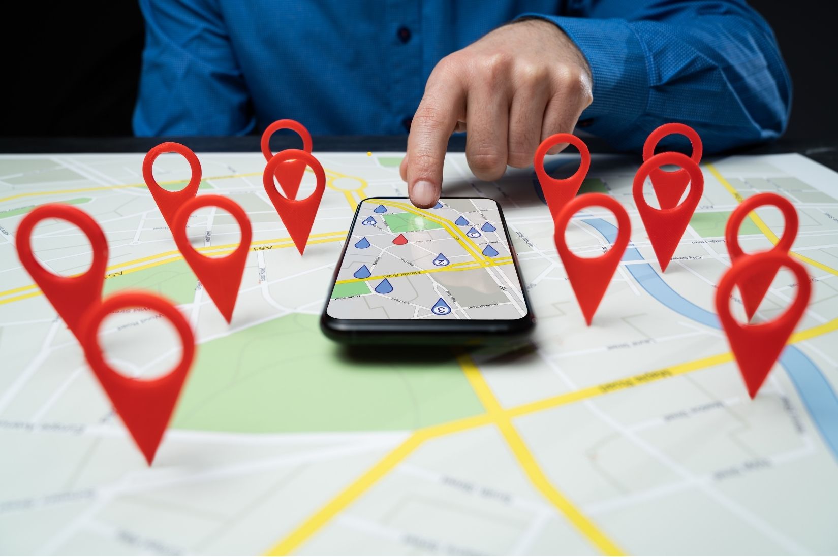 Map pins on a printed map next to a phone showing local results